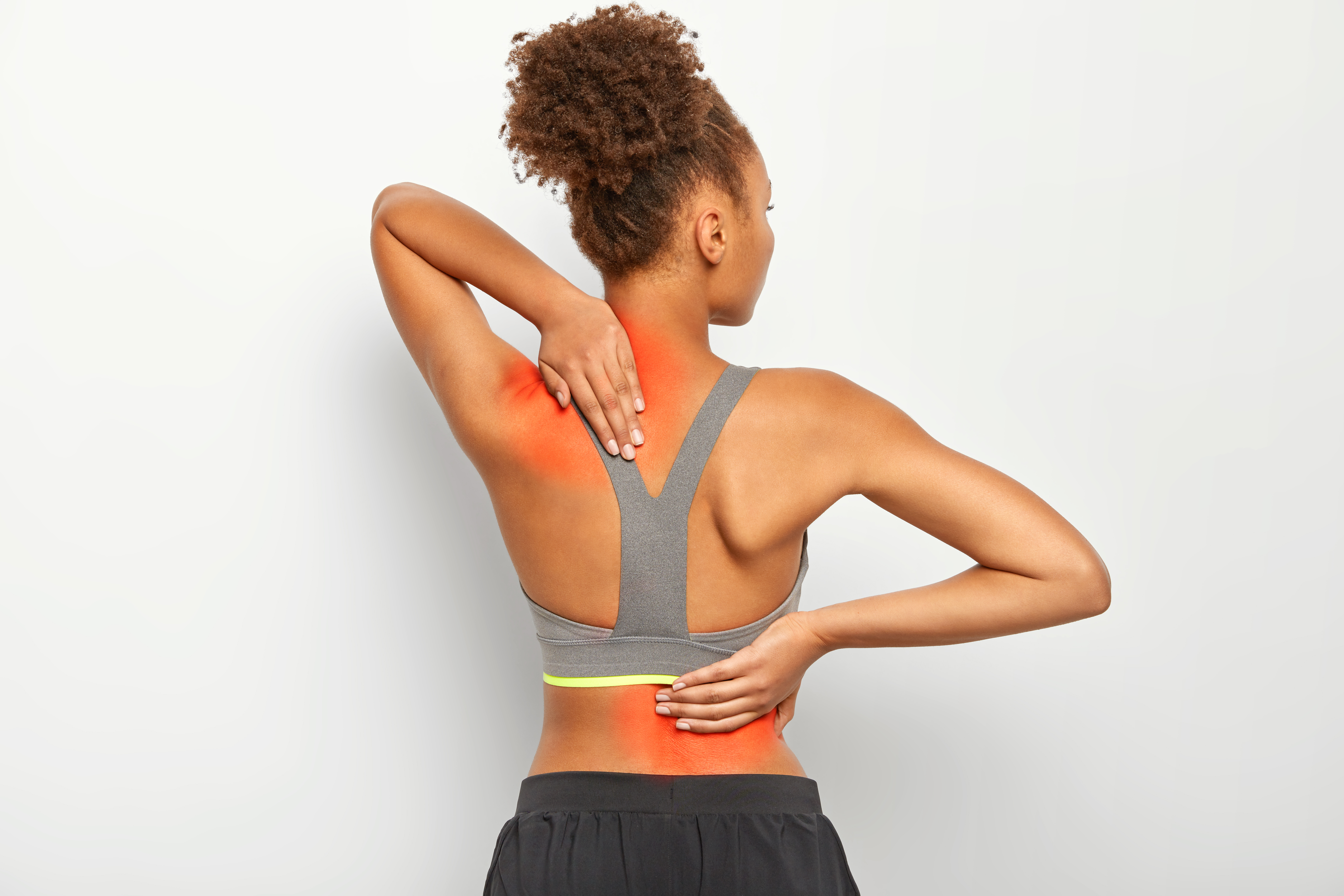 Faceless curly woman suffers from spine pain, has injury after overtraining, wears sport bra, shows location of inflammation, leads sporty lifestyle, isolated on white background. Chronic disease